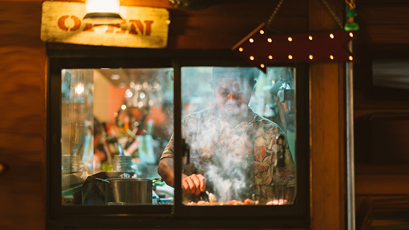 An owner of a Japanese style pub is cooking Japanese food in the kitchen of his shop.
